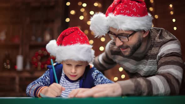 Boy and Male Parent Writing Wishes List Letter at Christmas Eve