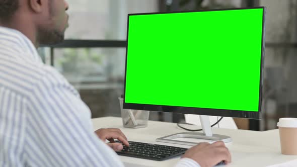 Rear View of African Man Using Desktop with Green Chroma Key Screen