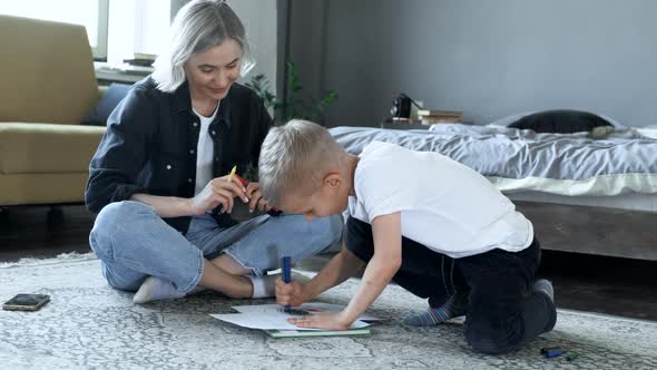 A Young Mother and a Baby Boy Are sitting on the Floor, The Boy Is Drawing with Felt-Tip Pens