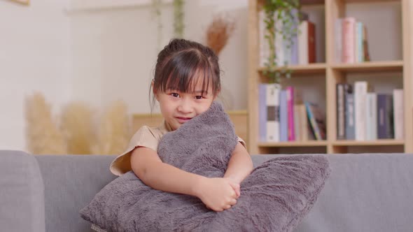 Adorable little girl sitting on couch hugging pillow smile looking at camera