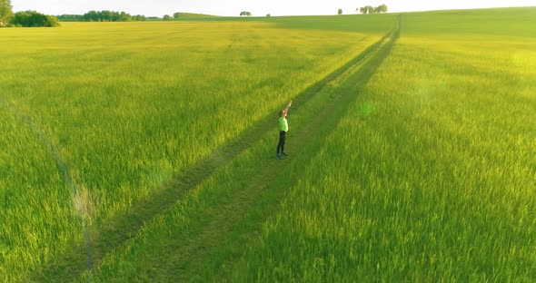 Sporty Child Standing in Green Wheat Field with Raised Hands Up