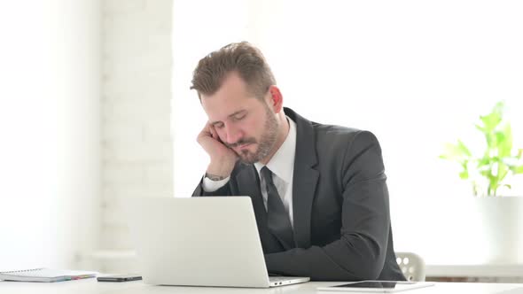 Young Businessman Falling Asleep While Working on Laptop in Office