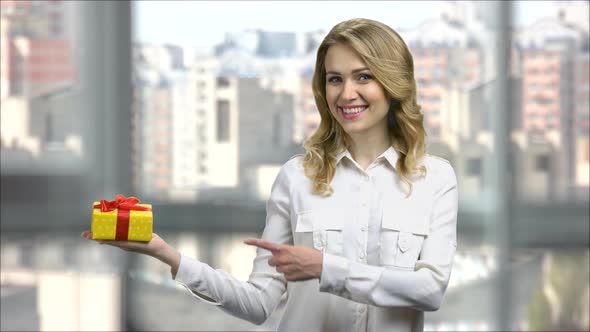 Young Happy Business Woman Holding Gift Box and Pointing at It