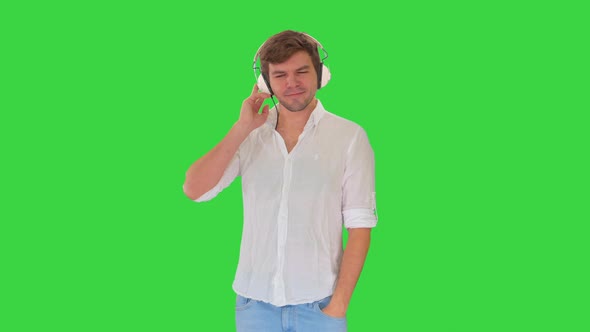 Casual Young Man Listening To Music Holding Headphones By His Hand on a Green Screen, Chroma Key.