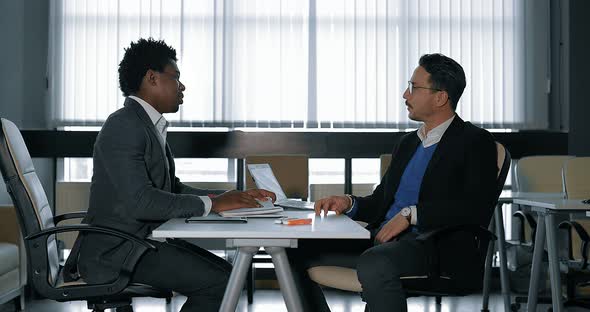 Two Young Businessman Talking at Desk in Office