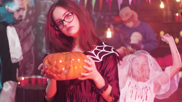 Teenage Girl Dances in Slow Motion with a Carved Pumpkin in Her Hand at a Halloween Party