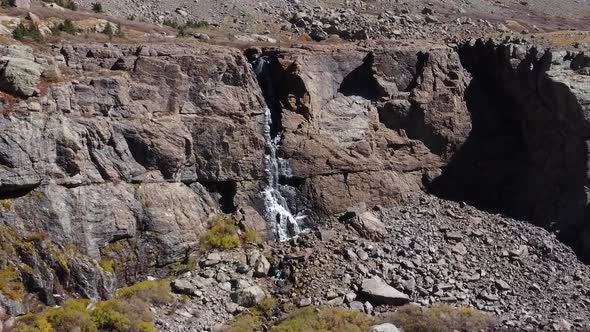 Flying through trees over Colorado mountain lake towards Willow Lake snowmelt waterfall, Aerial