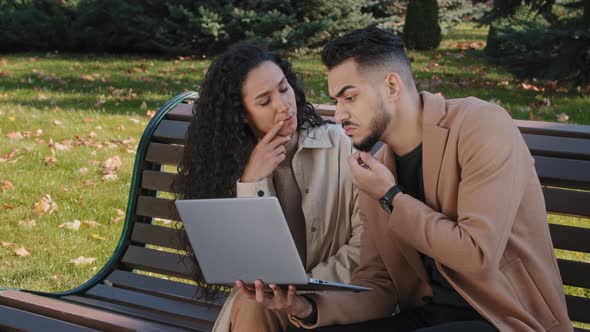 Young Hispanic Couple Sitting Together on Bench in Autumn Park Guy and Girl Thoughtfully Looking at