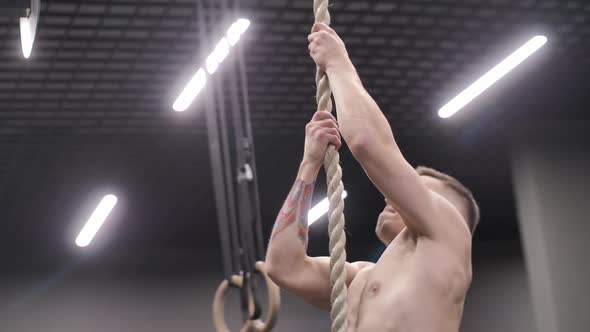 Athletic Man Climbing on a Rope, Crossfit Training Workout in Gym