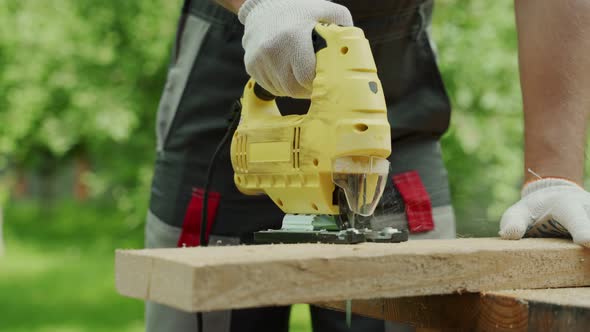 Closeup Male Carpenter Cuts a Wooden Board Using an Electric Jigsaw