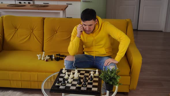 Young Man Sitting on Yellow Sofa and Playing Chess in Room