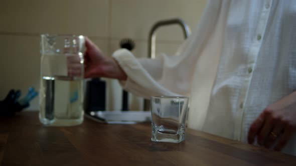 Closeup Female Hands Pouring Water Into Glass From Jug at Kitchen