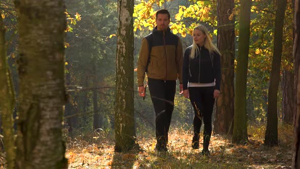 A Hiking Couple Walks Through a Forest on a Sunny Day - Front View