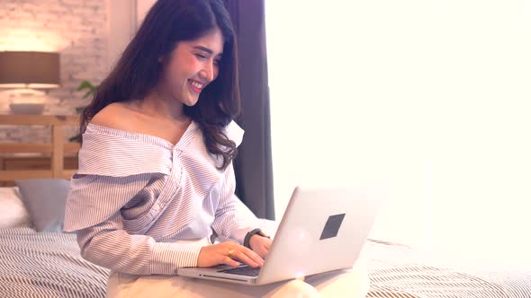 Happy Young Asian Girl on Bed While Making a Video Call with Phone and Waving in Bedroom at Home