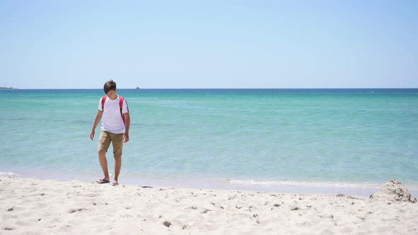 Eenager on the Background of the Azure Sea Walks Along the Beach on a Sunny Summer Day