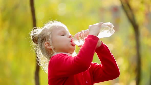 Little girl drinks clean water in the outdoors. Little girl drinks clean water in autumn Park.