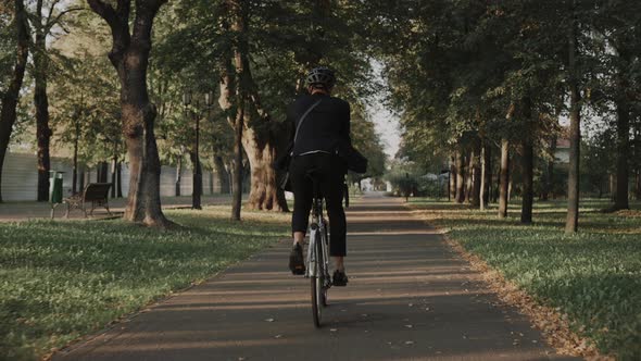 Young Man Riding a Bike in City Park Wearing Business Suit and Helmet Back View