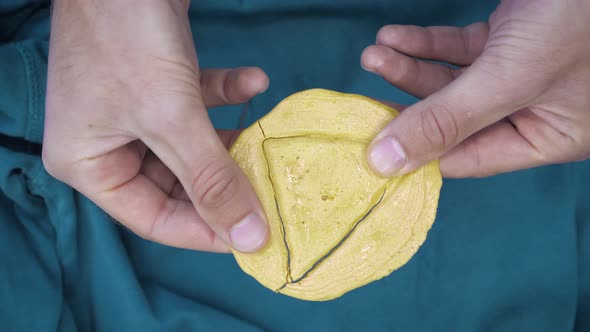 Man hands breaking Dalgona candy cookies in form of triangle.