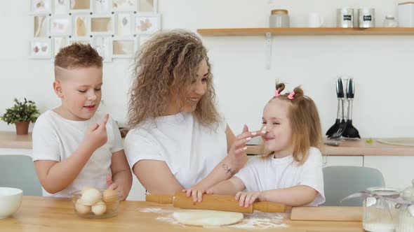 Mom Paints the Children's Noses with White Flour While They All Roll Out the Dough in the Kitchen in