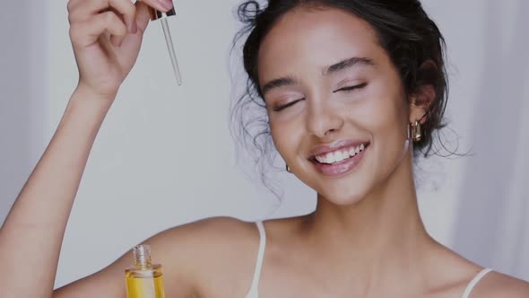 Beautiful Girl with Perfect Skin Dropping Oil Serum in Front of Her Face and Smiling