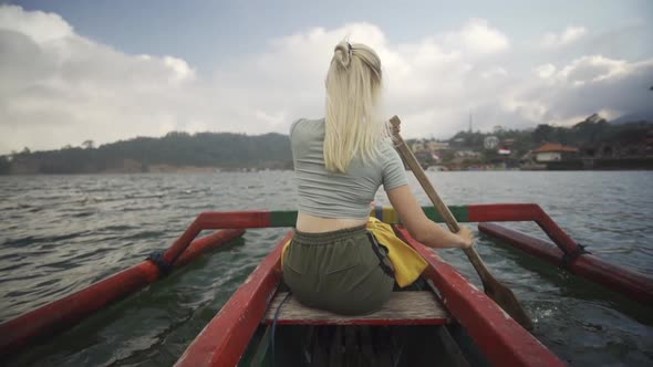 Blond Woman Rowing Outrigger With Oar In Bali