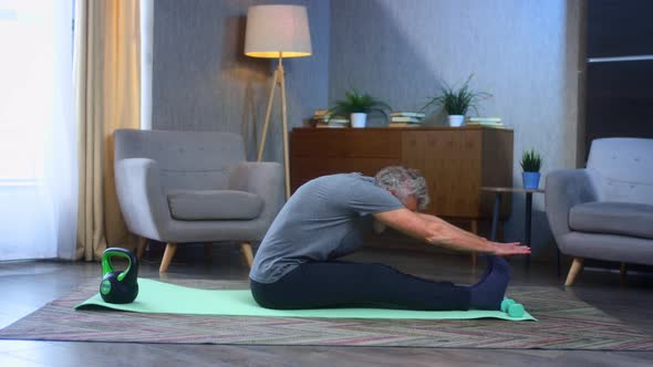 Grayhaired Senior Man Stretches at Home on a Yoga Mat