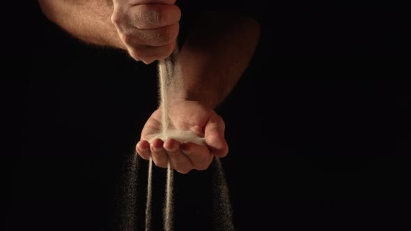 Stream of Dry Sand Pours Into Palm of Man and is Spilling Through His Fingers on Black Background