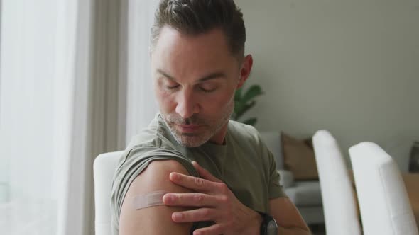 Portrait of caucasian man with vaccinated shoulder smiling and showing ok sign at home