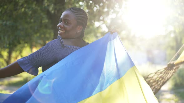 Medium Shot Happy African American Plussize Woman Spinning with Ukrainian Flag in Sunrays Smiling