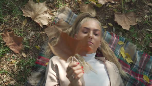 Smiling female lying on plaid with dry leaf in park