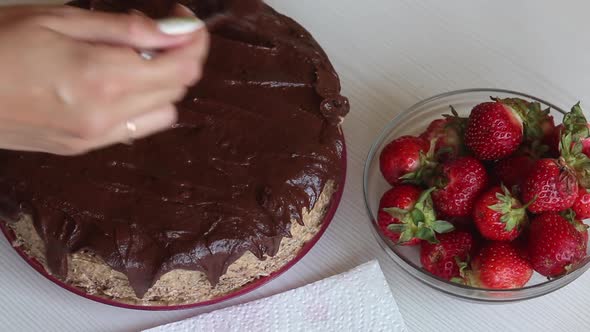 A Woman Applies Chocolate Ganache To A Sponge Cake.