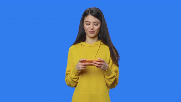 Portrait of Pretty Brunette Enthusiastically Plays a Game on Smartphone