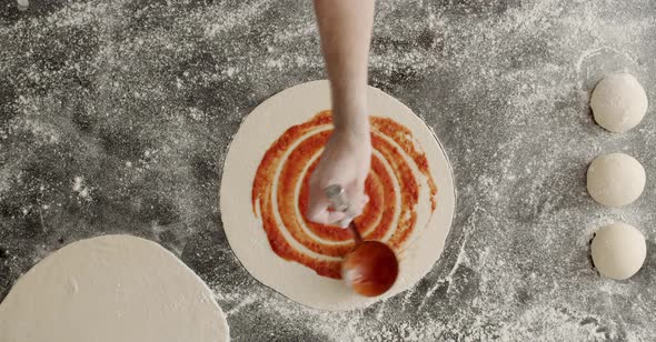 Crop chef smearing tomato sauce on pizza