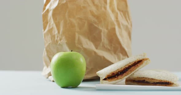 Peanut butter and jelly sandwich with apple and paper bag against white background