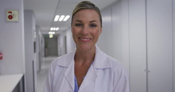 Portrait of caucasian female doctor standing in corridor laughing looking at camera