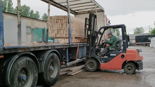 A Forklift Unloads Wooden Boards  Moving While Approaching the Goods to Unload It While Raining