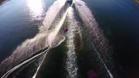 Aerial birds-eye drone view of a man wakeboarding behind a boat.