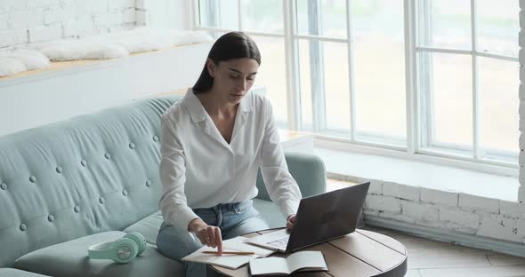 Focused Young Woman Student Preparing for Exams Using Laptop and Sitting Sofa