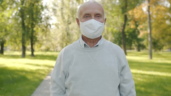 Slow Motion Portrait of Senior Man Wearing Medical Face Mask Standing in Summer Park Alone