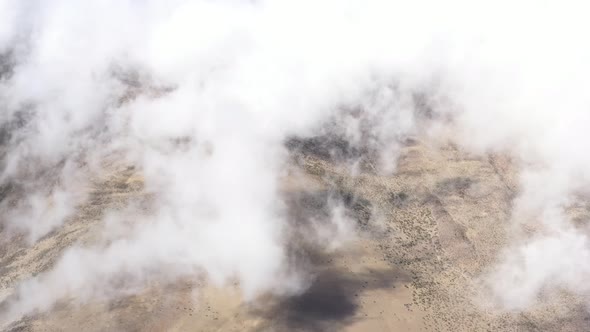 Flying above white clouds showing a stunning view of clouds slowly moving over the barren desert 