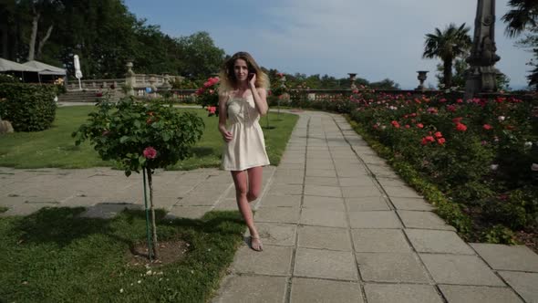 Girl Walking Along a Narrow Path Along a Beautiful Lawn with Pink Flowers