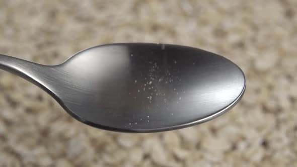 Filling a metal spoon with oatmeal in slow motion over a rotating heap