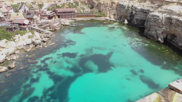 Low angle aerial shot over pier in Anchor Bay, showcasing Popeye Village surrounded by Turquoise sea