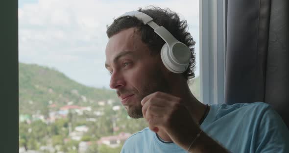 Handsome Relaxed Young Bearded Man in Audio Headset Listening to Audio Book or Music Standing By