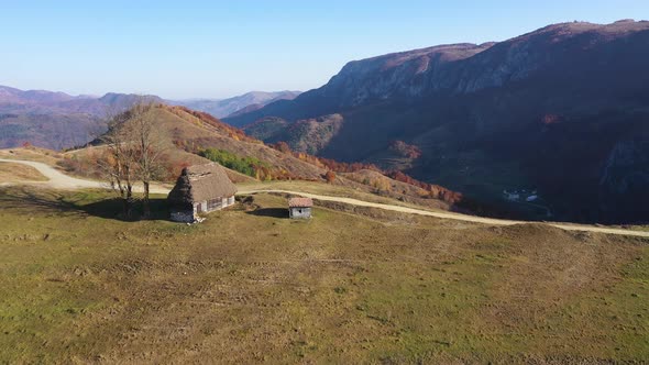 Flying Above Autumn Countryside Mountain Landscape with Wooden Houses, Thatched Roof and Dirt Road