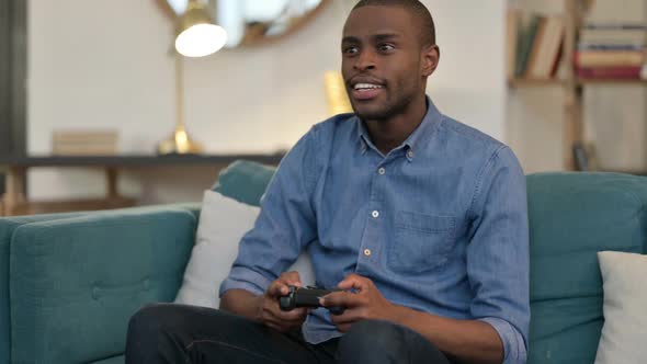 Young African Man Celebrating Success on Video Game on Sofa