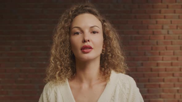 Close Up Portrait of a Confident Caucasian Curly Woman on a Brick Wall Background