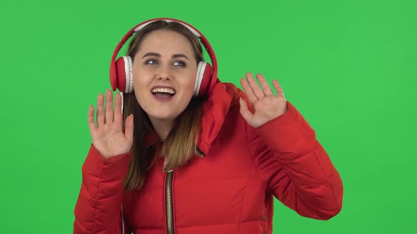 Portrait of Lovely Girl in a Red Down Jacket Is Dancing and Enjoying Music in Big Red Headphones