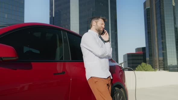 Red SUV Electric Car Plugged to Charging Station in Urban Downtown Background alt