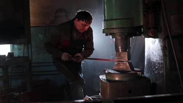 Focused Man Blacksmith Thinning a Hot Oblong Piece of Metal Under an Automatic Press